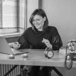 A young woman working on her laptop in a vintage-style office setting.