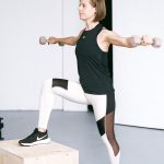 Woman performing fitness exercise with dumbbells in a gym setting, showcasing strength and balance.